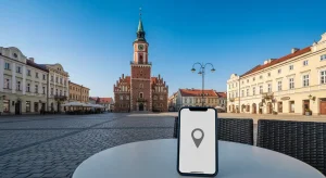 Rynek starego miasta w Rzeszowie z ratuszem i wieza zegarowa w swietle dnia, w tle kamienice, na pierwszym planie smartf