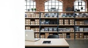 Uporządkowane półki z produktami e-commerce w jasnym warszawskim magazynie, laptop i tablet symbolizujące kategorie skle